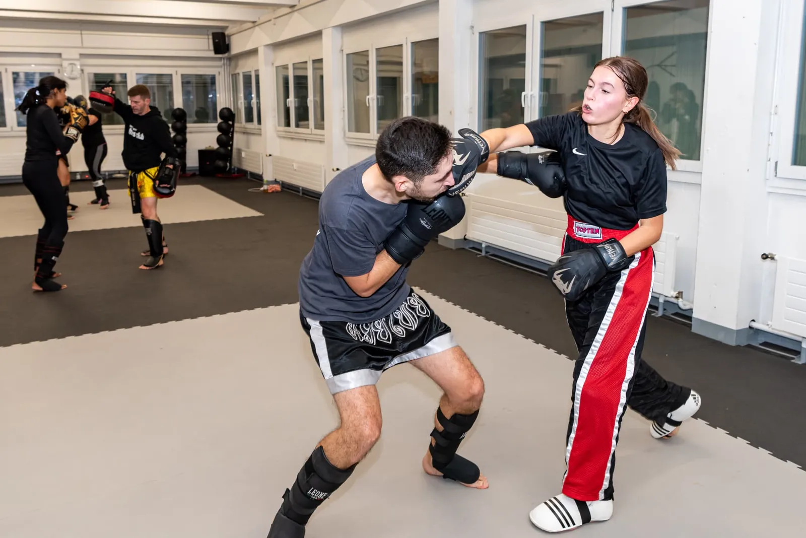 Frau schlägt mit Boxhandschuhen auf die Pratzen des Trainers beim Kickboxtraining